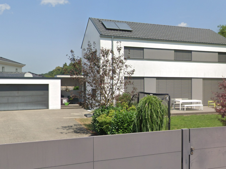 Modernes Haus mit Solarzellen, Garage und Gartenmöbeln im Freien.