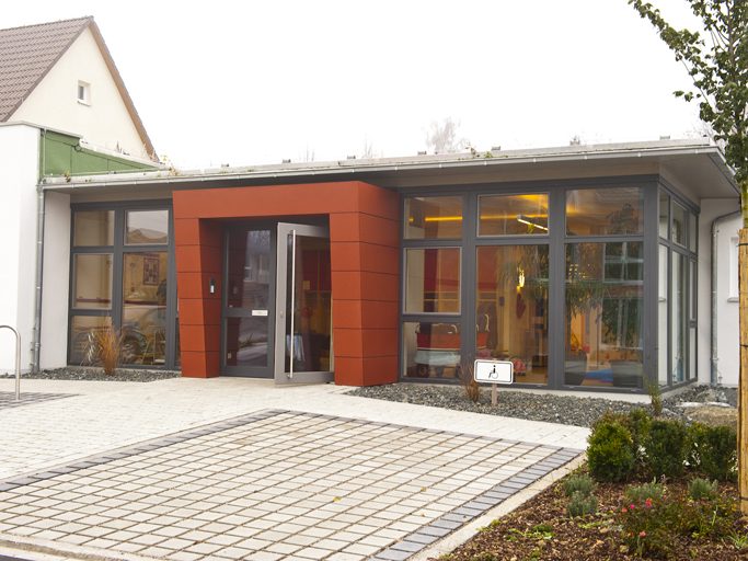 Modernes, weißes Wohnhaus mit Garage und grüner Umgebung unter bewölktem Himmel.