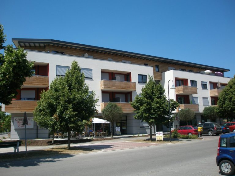 Moderne Wohnanlage mit mehreren Etagen und grünen Bäumen davor.