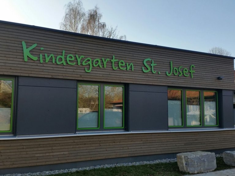 An der Außenwand eines Kindergartens steht "Kindergarten St. Josef" in grünen Buchstaben.