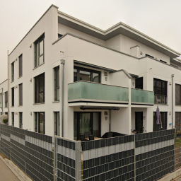 Modernes, mehrstöckiges Wohngebäude in Weiß mit Balkonen und einem Sichtschutz aus Stein.