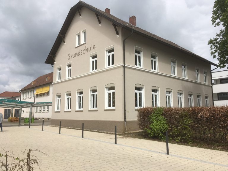 Historisches Gebäude mit vielen Fenstern und grüner Bepflanzung im Vordergrund.