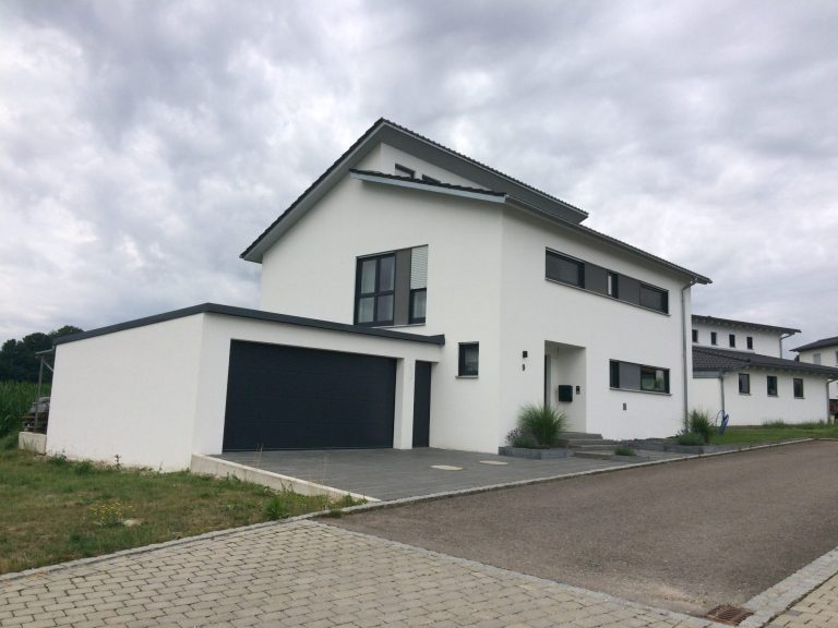 Moderne, zweigeschossige, weiße Wohnhaus mit Garagenanbau und grauem Pflasterweg.