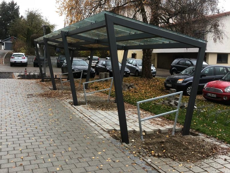 Ein überdachter Parkplatz mit mehreren abgestellten Autos und Laub auf dem Boden.