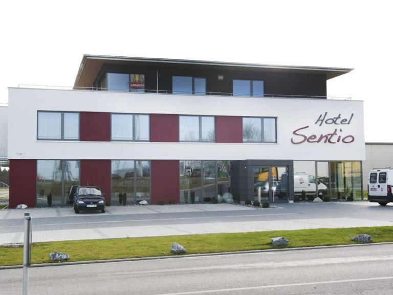 Moderne Hotelfassade mit roten und weißen Elementen und Parkplatz davor.