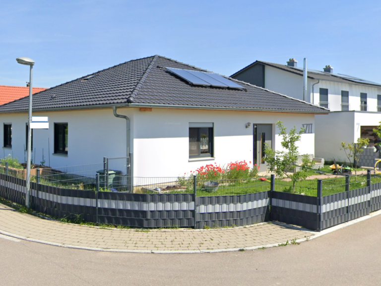 Modernes Haus mit Solaranlage, umgeben von einem gepflegten Garten und Zaun.