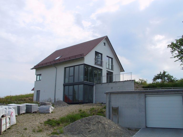Moderner Hausbau mit großen Fenstern, rotem Dach und angrenzender Garage.