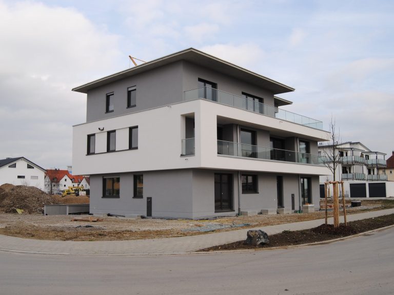 Modernes, mehrstöckiges Wohnhaus mit Balkon und grauer Fassade in einer Wohngegend.