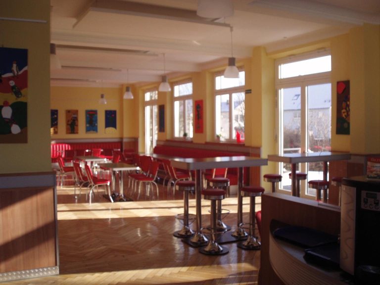 Helle Café-Umgebung mit roten Stühlen und großen Fenstern.