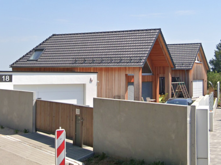 Moderne Wohnhäuser mit Holzelementen und Garagen, umgeben von einem Zaun.