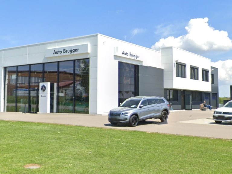 Moderne Autowerkstatt mit Glasfront und zwei Fahrzeugen vor einem geschlossenen Parkplatz.