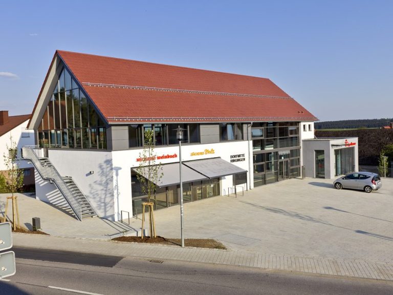 Modernes, weißes Wohnhaus mit Garage und grüner Umgebung unter bewölktem Himmel.