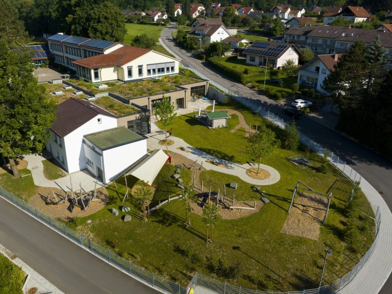 Luftaufnahme eines Spielplatzes mit Rutschen, Schaukeln und umliegenden Gebäuden.