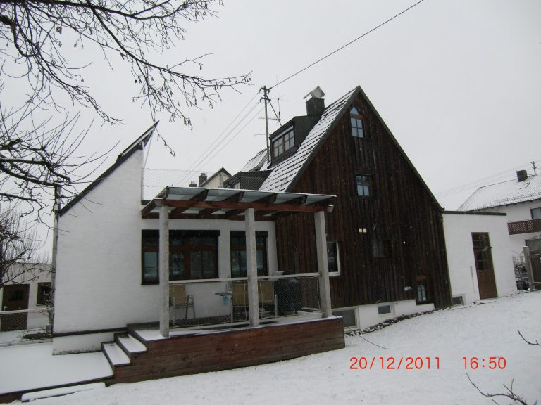 Moderner Hausbau mit großen Fenstern, rotem Dach und angrenzender Garage.