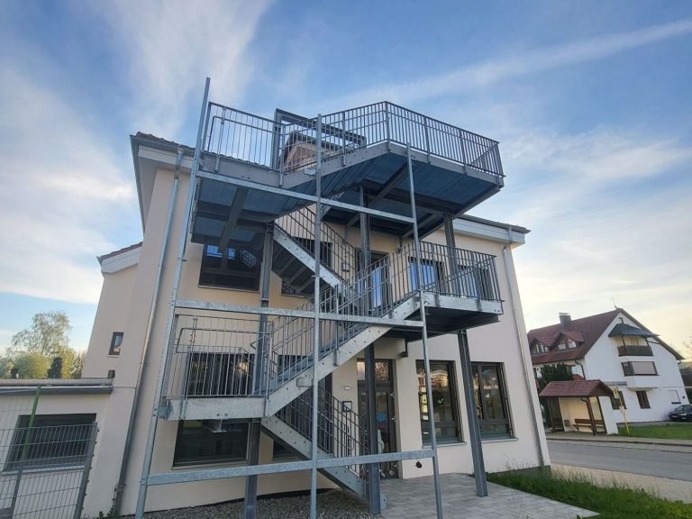 Modernes, weißes Wohnhaus mit Garage und grüner Umgebung unter bewölktem Himmel.