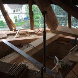 Blick auf das Dachgeschoss mit Holzbalken, Baugeräten und Baustellenumgebung.