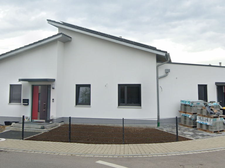 Einfamilienhaus mit roter Tür und neuem Garten, umgeben von einem niedrigen Zaun.