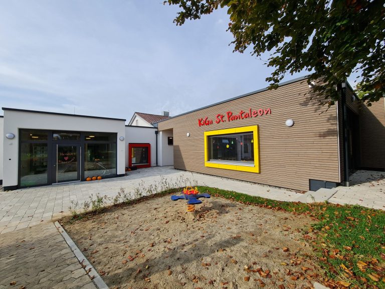 Modernes Gebäude mit buntem Spielplatz und großzügigen Fenstern.